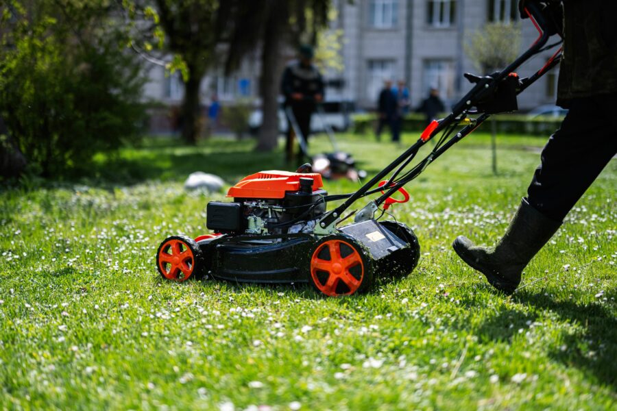 Communal services gardener worker man using lawn mower for grass cutting in city park.